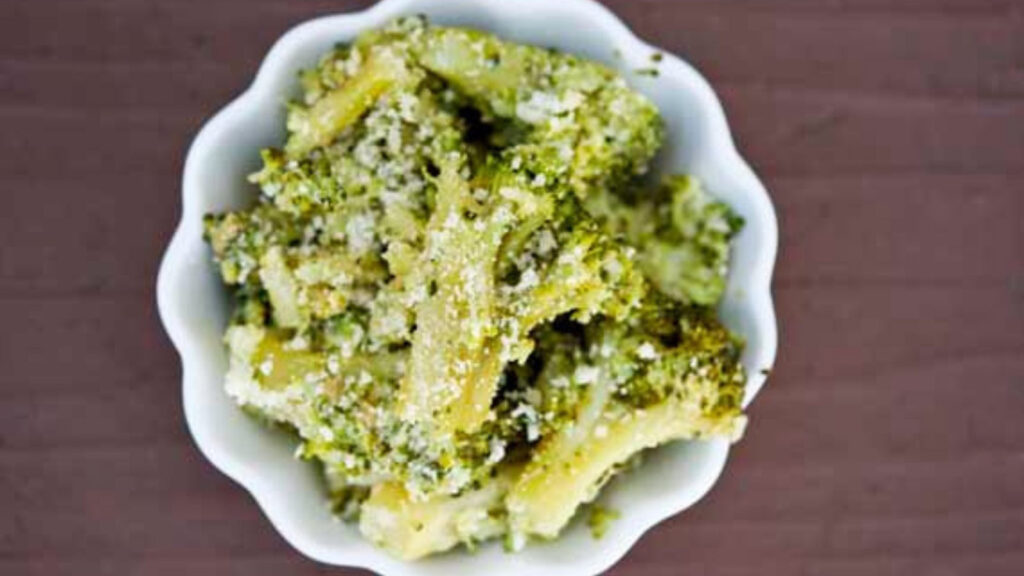 A white bowl sits filled with this Garlic Broccoli Recipe. You can see the specs of white parmesan coating the bright green broccoli florets.