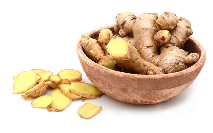 A wood bowl filled with fresh ginger. Slices of ginger lay next to it.