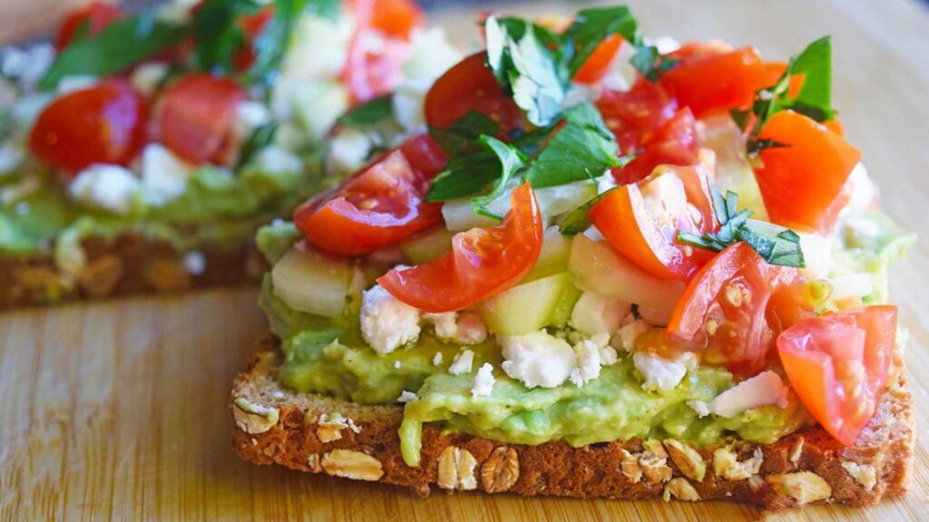 A closeup of a piece of Greek Avocado Toast on a cutting board.