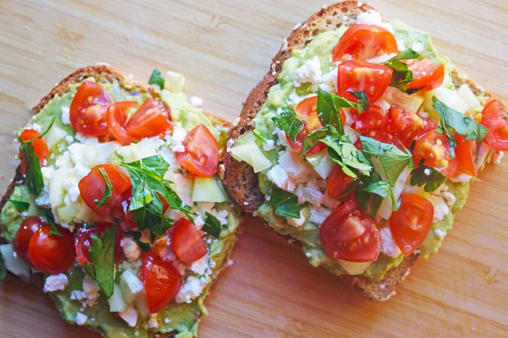 A closeup of just-made Greek avocado toast on a cutting board.