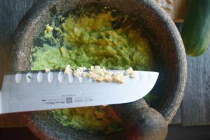 Adding minced garlic to the mortar for grinding into the avocado.