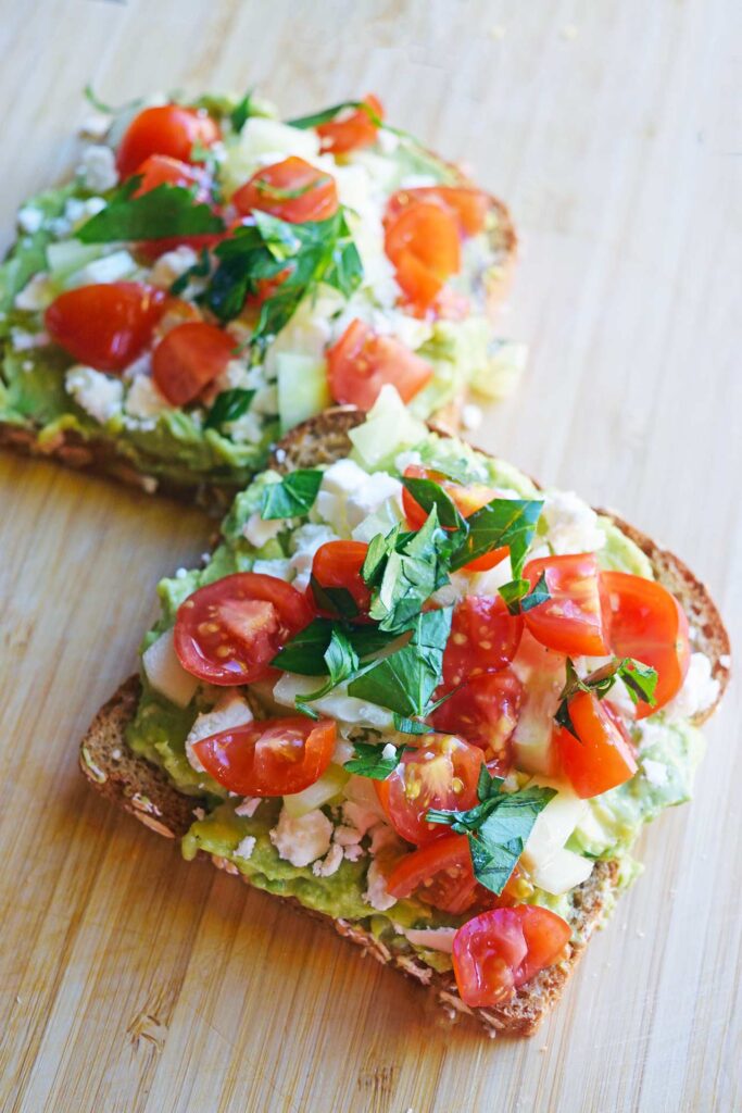 Two slices of Greek avocado toast laying on a cutting board.