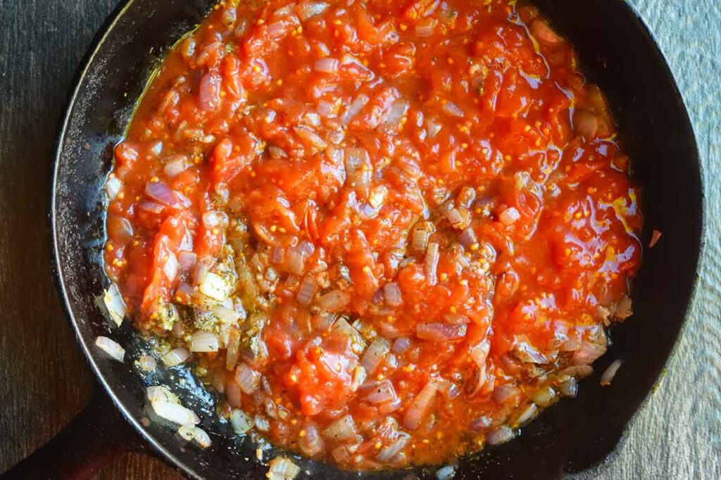 Diced tomatoes added to onions and garlic in a cast iron skillet.