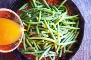 Broth being poured into the skillet with green beans.