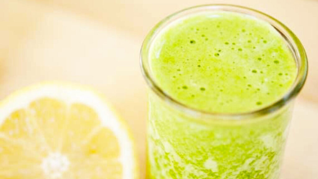 Green Lemon Pineapple Smoothie in a small glass sitting next to half a lemon.