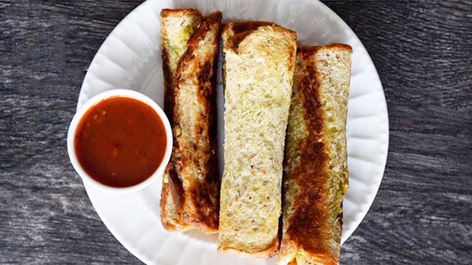 Grilled Cheese Roll Ups with a side of marinara for dipping on a white plate.