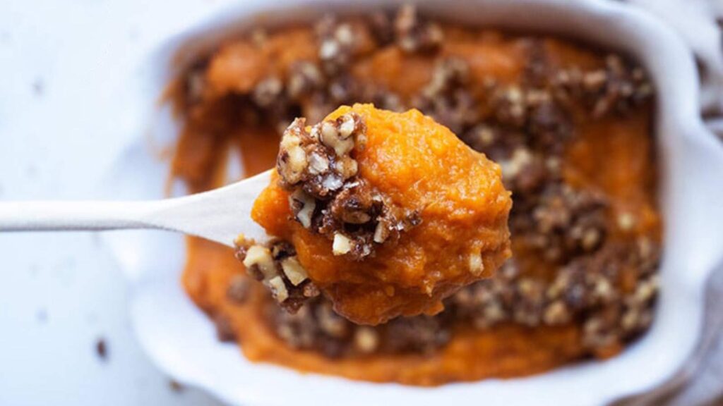 A spoon lifts some Healthy Sweet Potato Casserole up out of a white casserole dish.