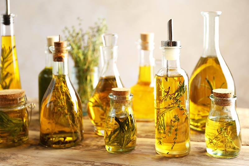 Glass bottles filled with oil and herbs sitting on a wood counter.