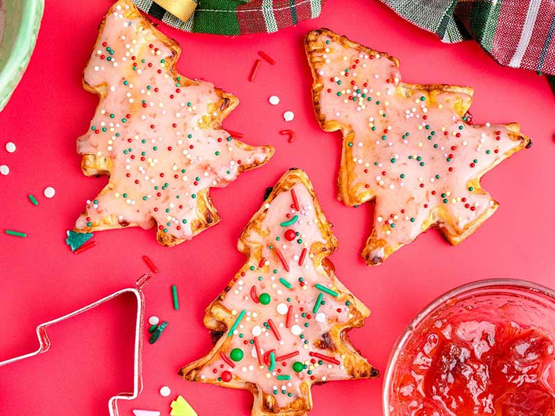 Christmas tree shaped pop tarts on a red surface.