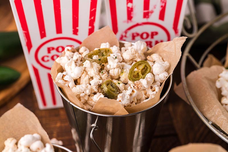 A tin of jalapeno popcorn topped with jalapeno slices.