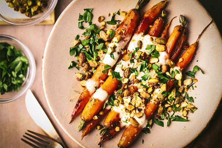 A plate holds six honey roasted carrots topped with fresh garnishes and sauce.