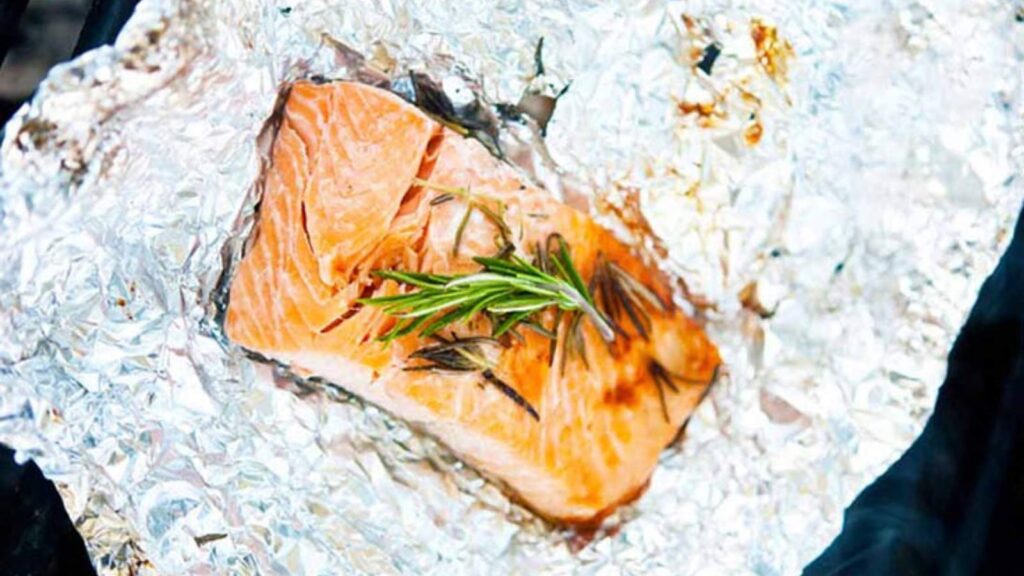 A hot coal salmon filet laying on foil on a grill.