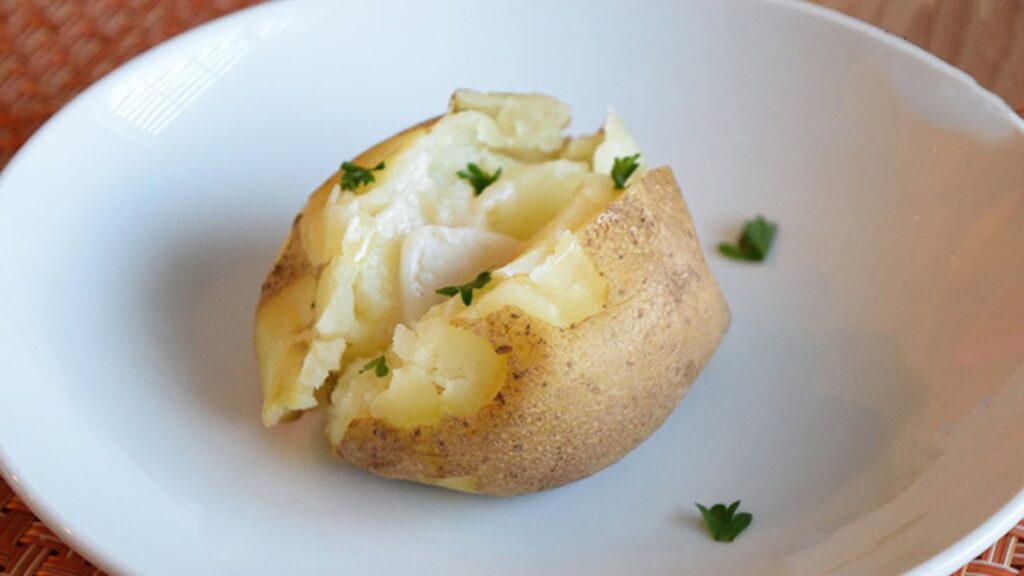 A single, Instant Pot baked potato in a bowl. It's cut open and has melting butter in it.