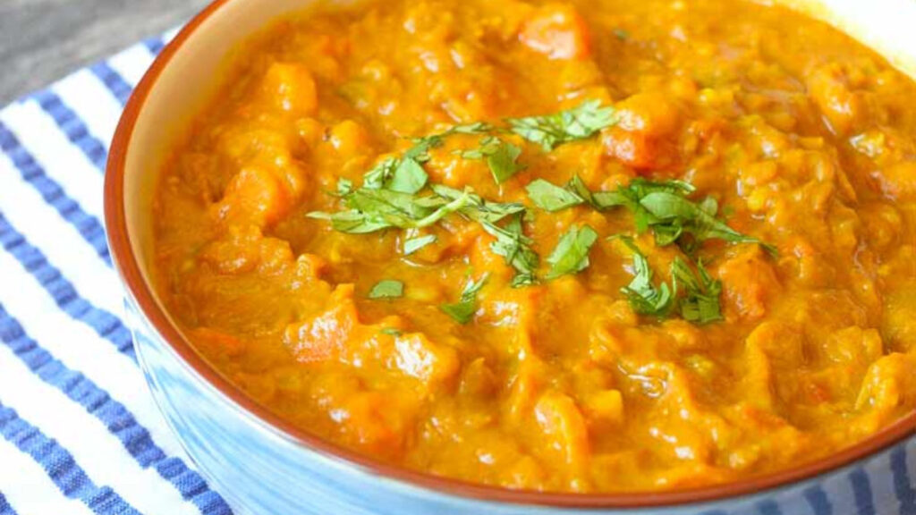 A bowl of orange colored curry lentils in a blue bowl.