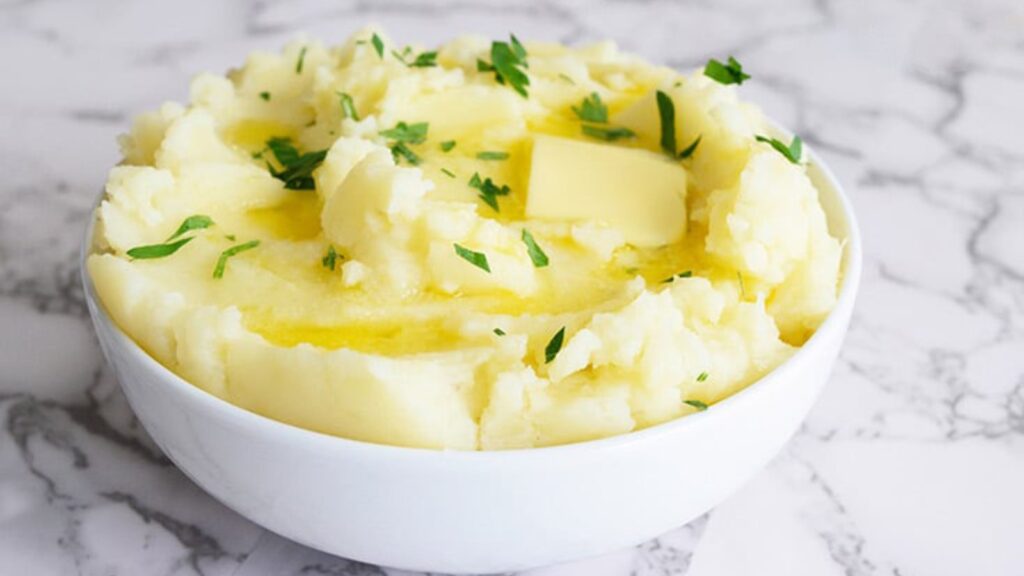 A white bowl full of Instant Pot mashed potatoes topped with melting butter.