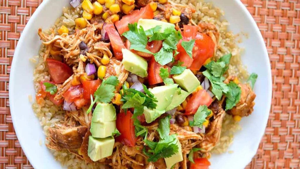 An overhead view of a white bowl filled with instant pot Mexican chicken topped with fresh tomatoes, avocado and cilantro.