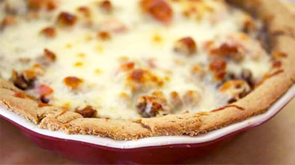 An Italian shepherds pie in a red pie pan. Melted cheese covered the entire surface of the pie filling.