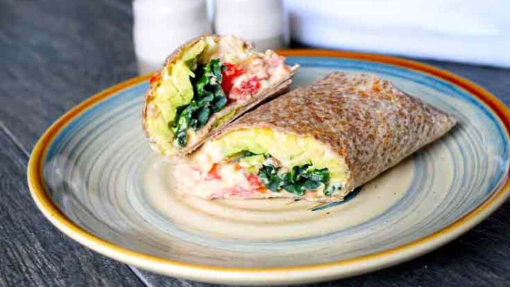 A Kale And Hummus Wrap, cut in half, laying on a plate.