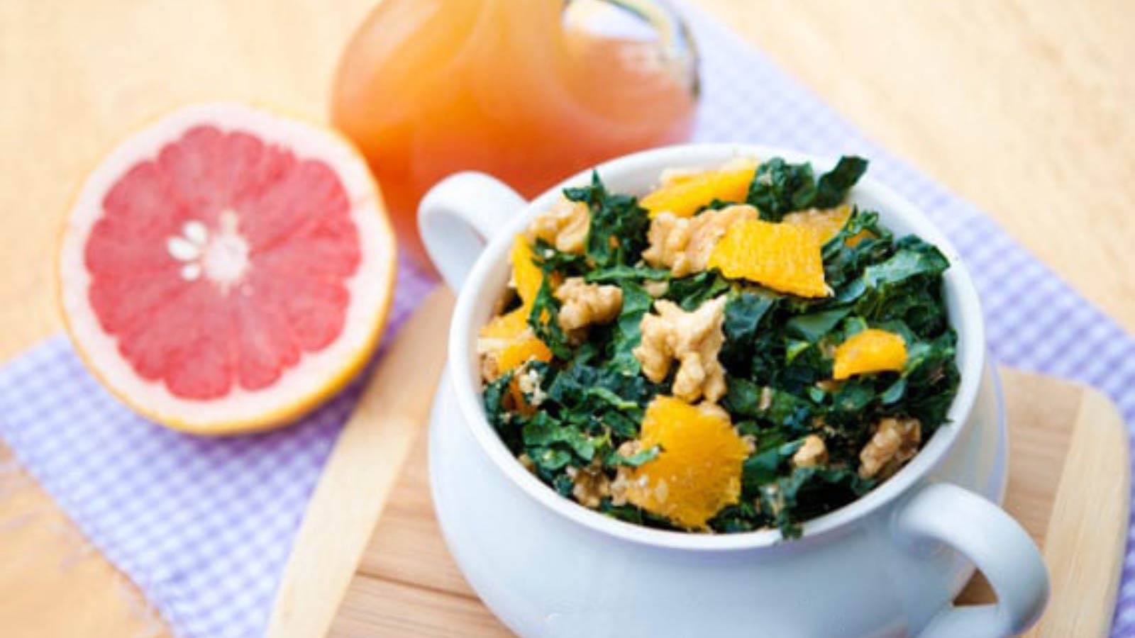 Spring Kale & Orange Salad in a white crock next to a bottle of grapefruit vinaigrette and half a fresh grapefruit.