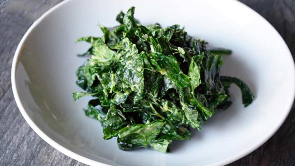 A white bowl holds a small serving of kale salad.