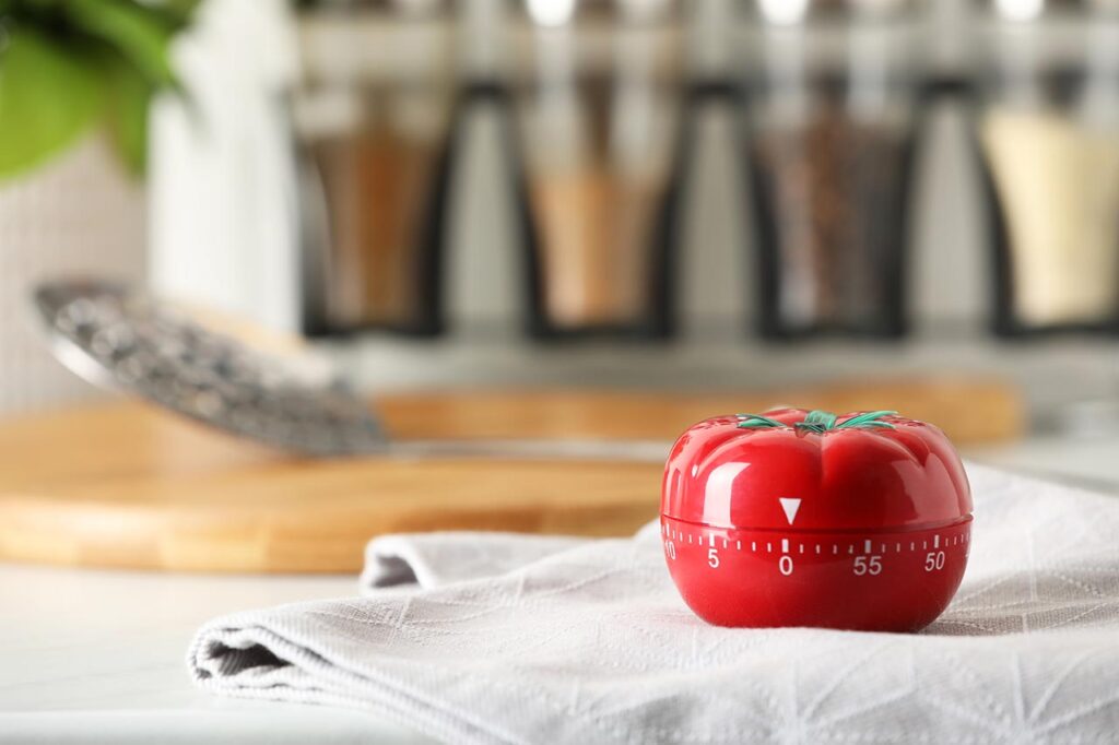 A red kitchen timer on a towel in a kitchen.
