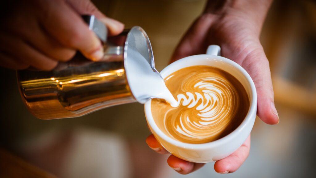 Milk being poured into a latte to make a pretty, squiggly design.