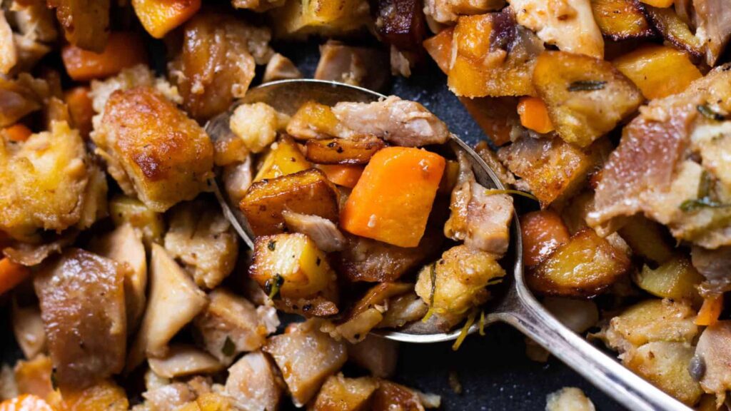A closeup of a spoon laying on a sheet pan filled and surrounded by leftover turkey hash.