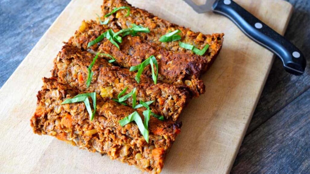 A side view of lentil loaf sliced on a cutting board and garnished with fresh greens.