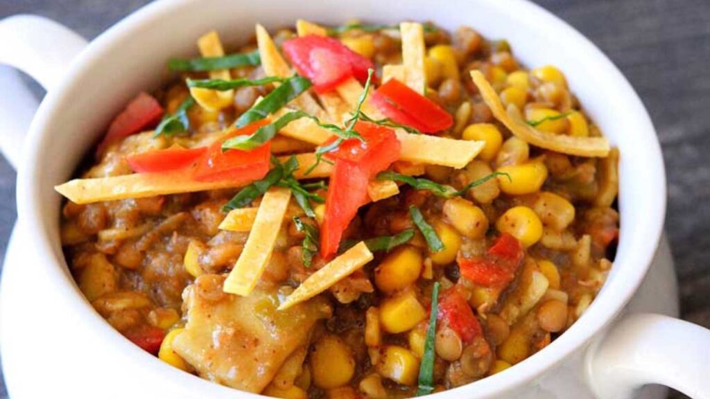 A closeup of a white crock filled with Lentil Tortilla Stew and garnished with chopped tomatoes, tortilla pieces and fresh cilantro.