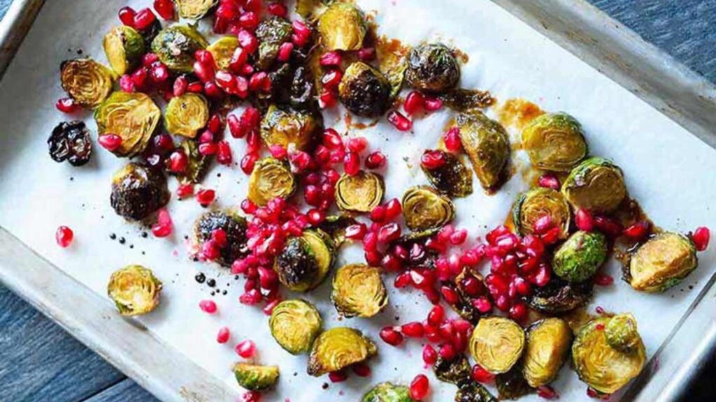 A sheet pan with Maple Roasted Brussels Sprouts and pomegranate arils on it.