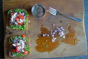 Feta cheese sprinkled over two slices of Mediterranean Avocado Toast on a cutting board.