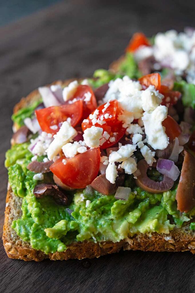 A side view of two slices of Mediterranean Avocado Toast on a cutting board.