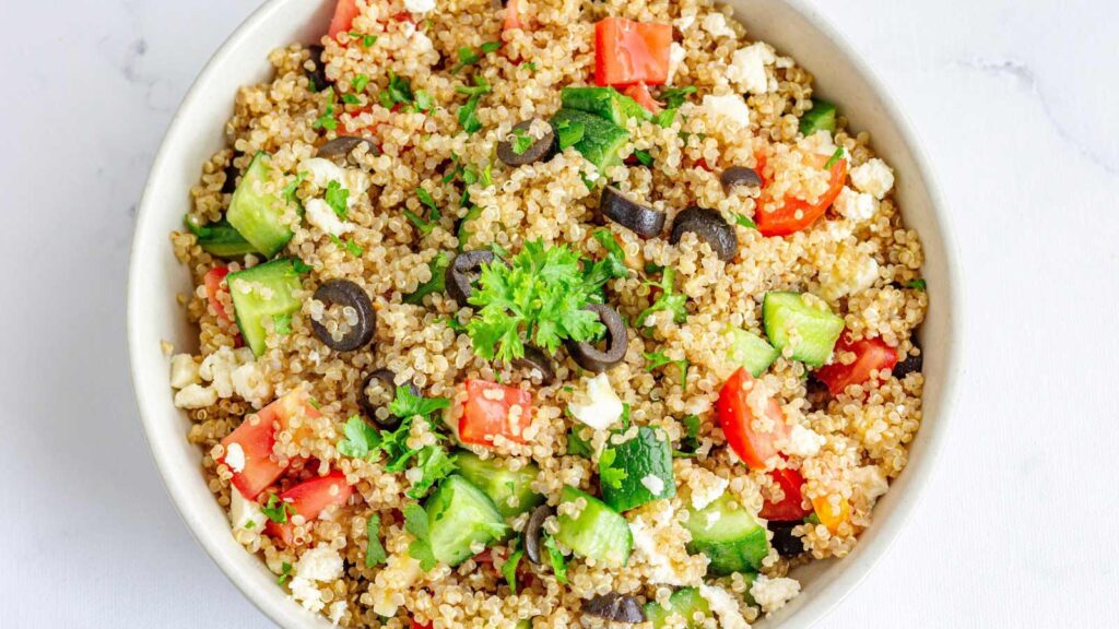 An overhead view of a white ceramic bowl filled with Mediterranean quinoa salad.