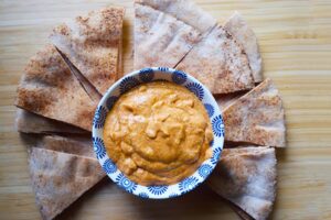 An overhead view of a bowl of dip surrounded by pita triangles.