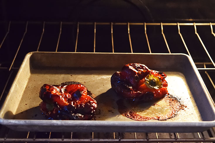Two roasted red bell peppers on a sheet pan in an oven.