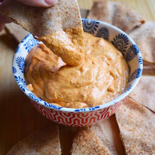 A side view of a hand dipping pita bread into a bowl of dip.