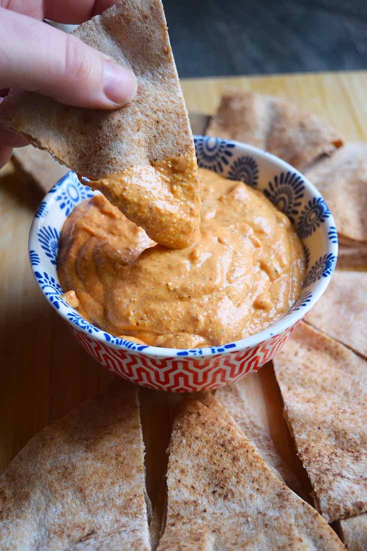 A side view of a hand dipping pita bread into a bowl of dip.