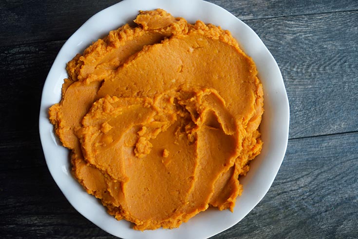 Sweet potato mash transferred to a white, fluted, ceramic pie pan.