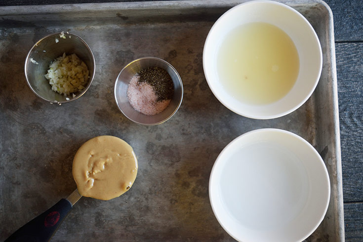 Dressing ingredients collected on a sheet pan in individual bowls.