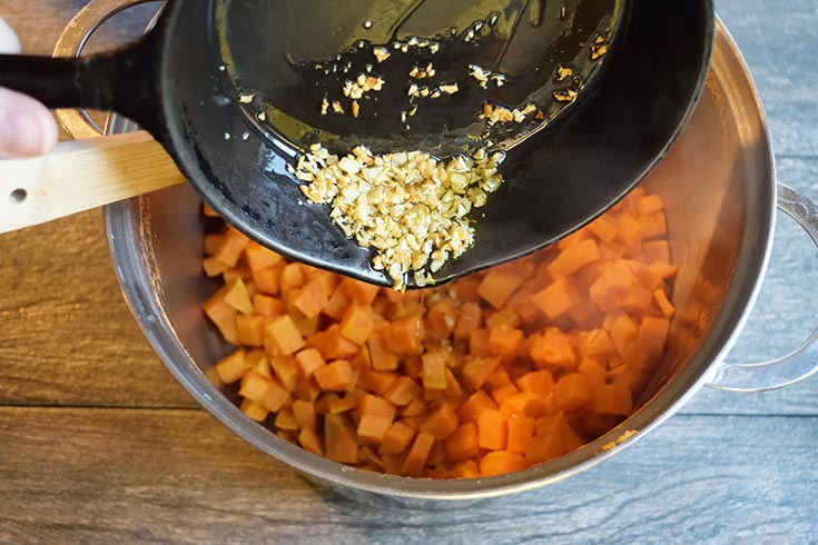 Adding sautéd garlic to the pot of sweet potoates.