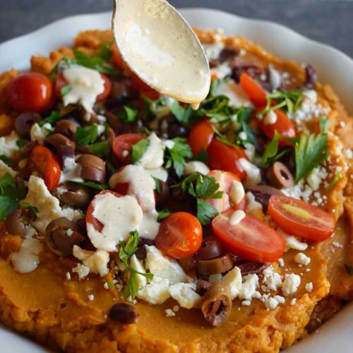 A spoon drizzled tahini dressing over the Mediterranean-Style Sweet Potato Casserole.