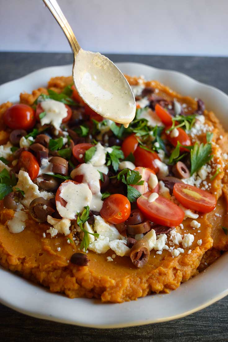 A spoon drizzled tahini dressing over the Mediterranean-Style Sweet Potato Casserole.