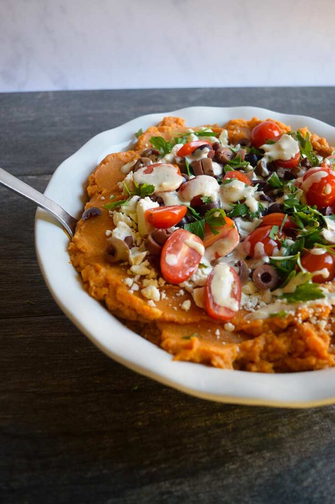 A serving spoon sits in the dish of Mediterranean-Style Sweet Potato Casserole.