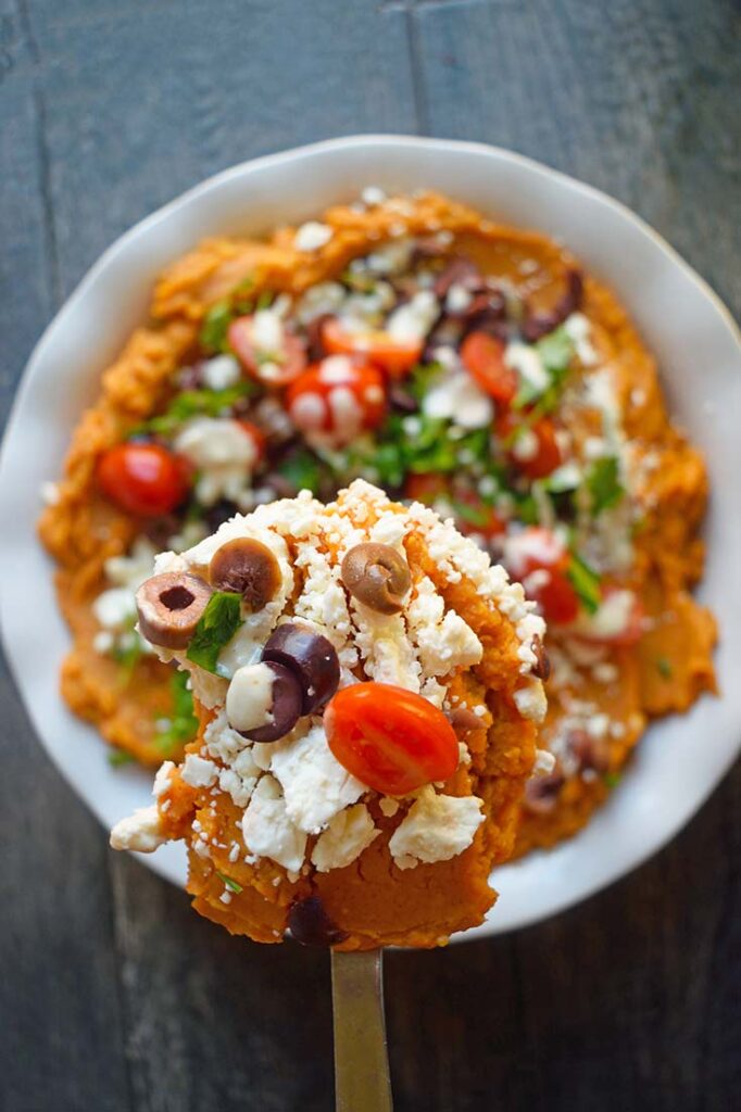 A serving spoon lifts up a serving of Mediterranean-Style Sweet Potato Casserole.