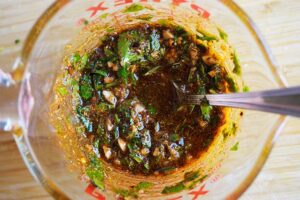 The herbs and spices mixed with the oil in a measuring cup.