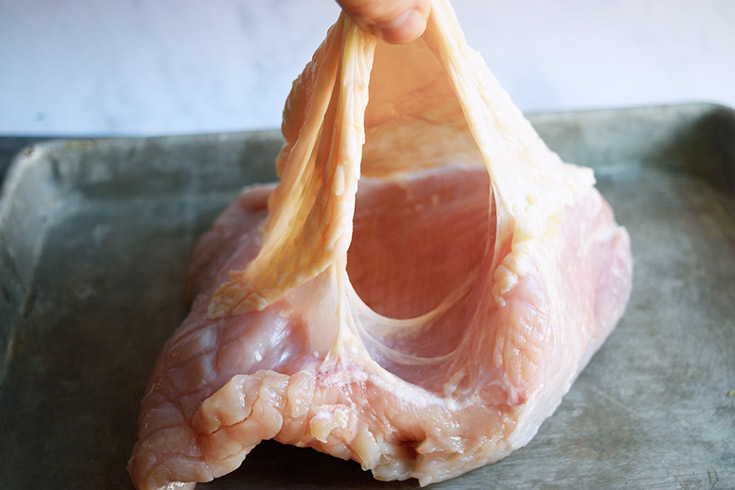 Lifting the skin of a turkey breast to show underneath.