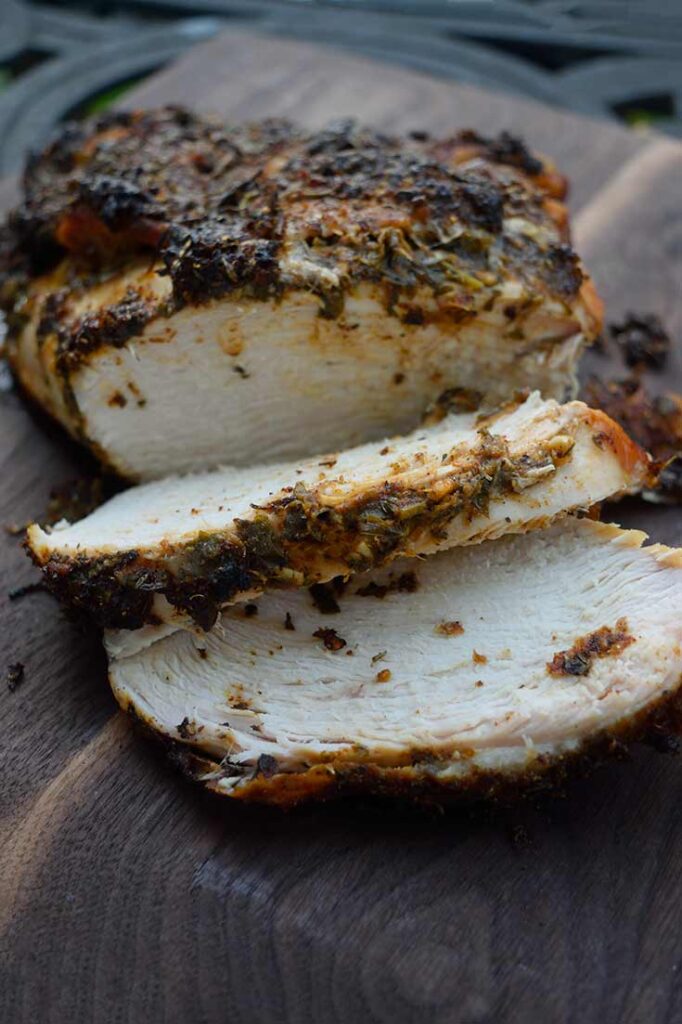 A front view of a Herb-Infused Mediterranean Turkey Breast laying on a cutting board with two slices carved.