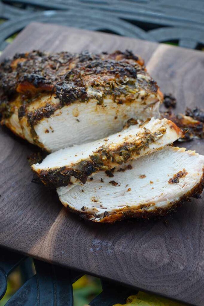 A side view of a Herb-Infused Mediterranean Turkey Breast on a cutting board that is partially carved.