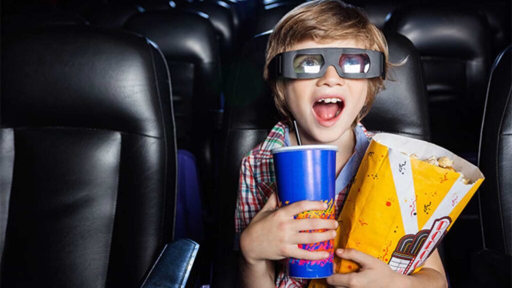 A young boy watching a movie holding a drink and a popcorn bag.