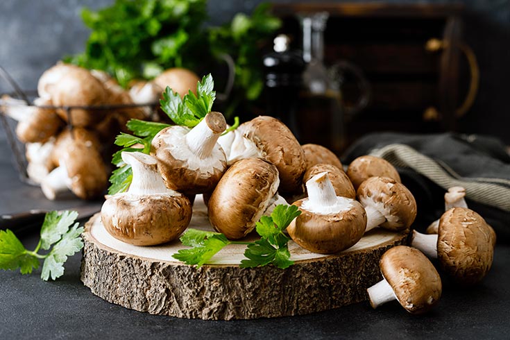 A pile of raw mushrooms with green parsley leave sprinkled on top.
